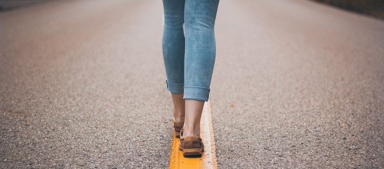 This is an image of lady's legs walking on the yellow line.