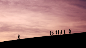 One man walking ahead while seven people follow him in a fair distance; delegate